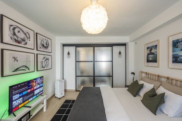 Une chambre d’hôtel moderne dotée d’un grand lit, d’un téléviseur à écran plat, d’œuvres d’art aux murs et d’une grande fenêtre offrant une vue panoramique.