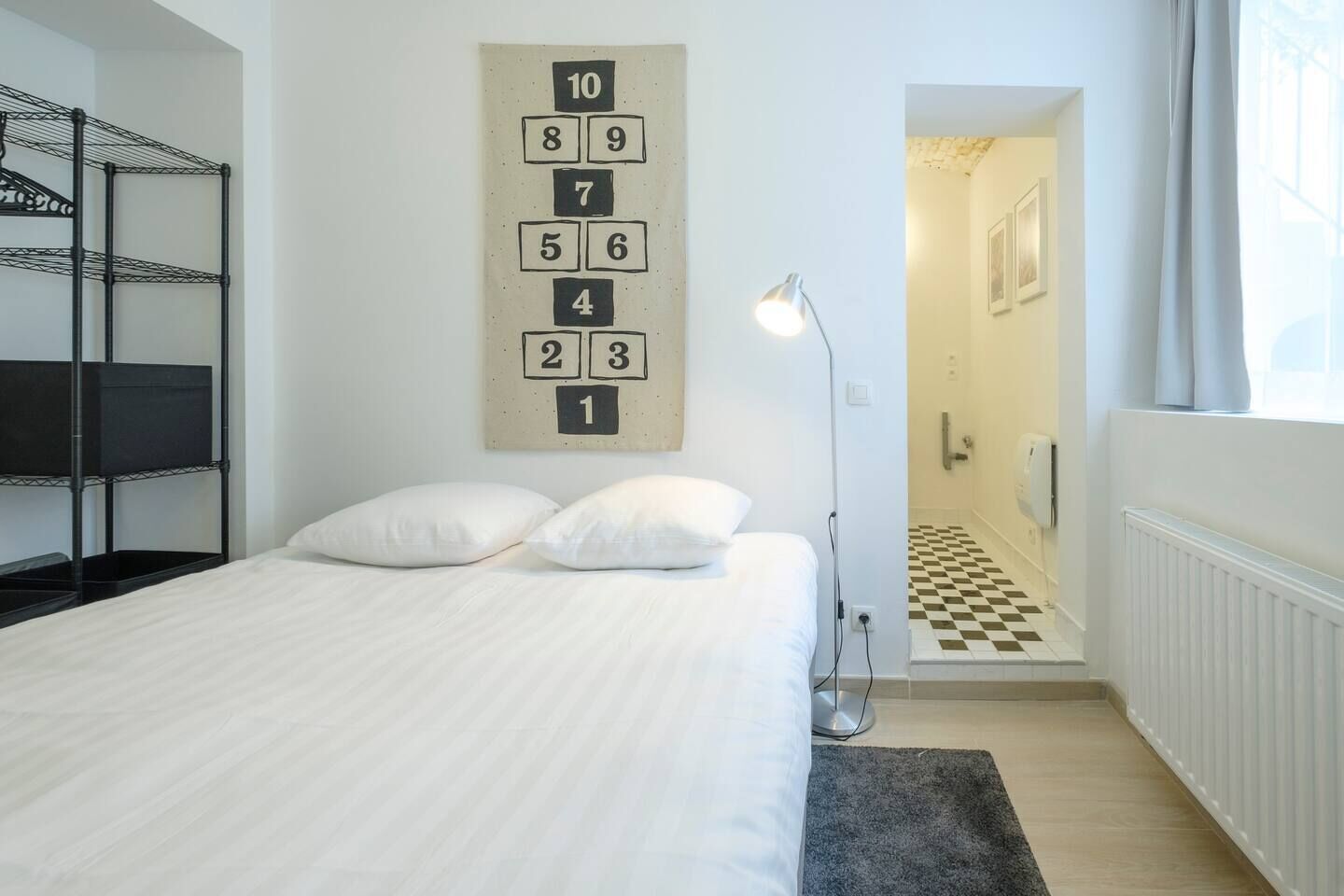 A hotel room with a bed, a number wall, a lamp, and a checkered floor.