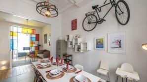 A dining area with a long table set for six, white chairs, and a bicycle mounted on the wall. - Boutique Duplex in Brussels - Superb Location (Molenbeek-Saint-Jean)