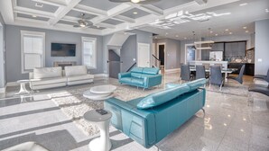 A spacious living area with a high ceiling, modern furniture, and a kitchen in the background. - Cloud IX | Luxury Home In North Beach Resort (North Myrtle Beach)