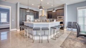 A modern kitchen with a central island, bar stools, and pendant lighting. - Cloud IX | Luxury Home In North Beach Resort (North Myrtle Beach)