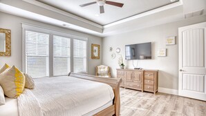 Une chambre à coucher avec un lit, un ventilateur de plafond, une commode, un téléviseur et une porte.
