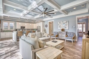 A spacious living room with a large sofa, coffee table, and two patterned armchairs. A ceiling fan and recessed lighting are visible.