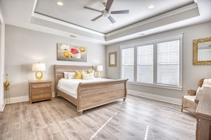 A bedroom with a wooden bed, a nightstand, a lamp, a painting, and a window with blinds.