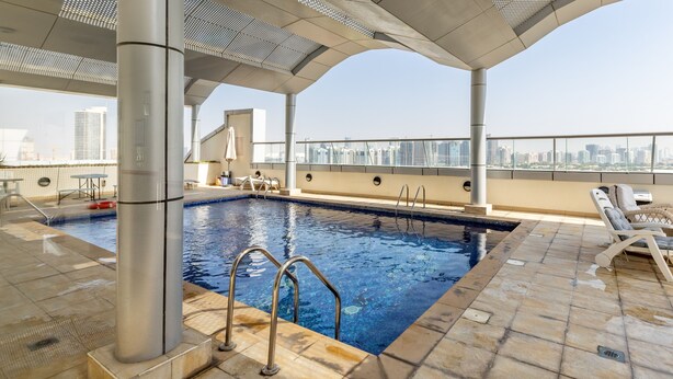 An indoor swimming pool with clear blue water, surrounded by tiled flooring and metal railings. - Waves - Cozy, Fully Furnished Studio in Dubai Sports City (Dubai)