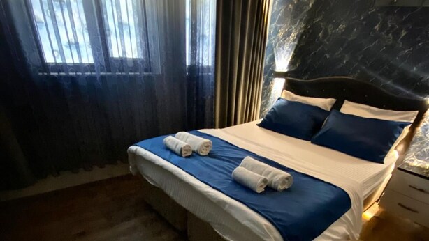 A neatly made bed with blue and white bedding, a wooden floor, and a window with curtains. - Yesil Hotel  (Bursa)