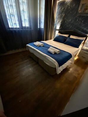 A neatly made bed with blue and white bedding, a wooden floor, and a window with curtains. - Yesil Hotel  (Bursa)