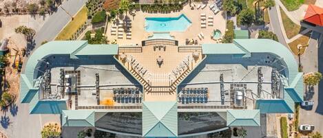 An aerial view of a hotel with a central swimming pool, multiple parking lots, and a distinctive green roof structure.