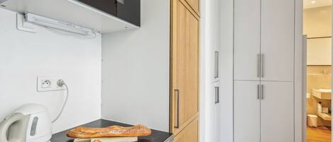 A kitchenette with a microwave, toaster, and a plate of pastries. There is a wooden cabinet and a white door in the background.