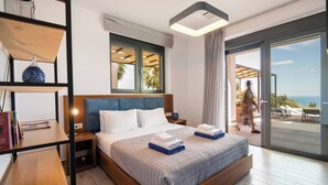 A modern hotel room with a large bed, a wooden nightstand, a bookshelf, and a large window with a view of the outdoors.