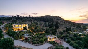 A modern villa with a spacious patio, surrounded by lush greenery and a hilly landscape.