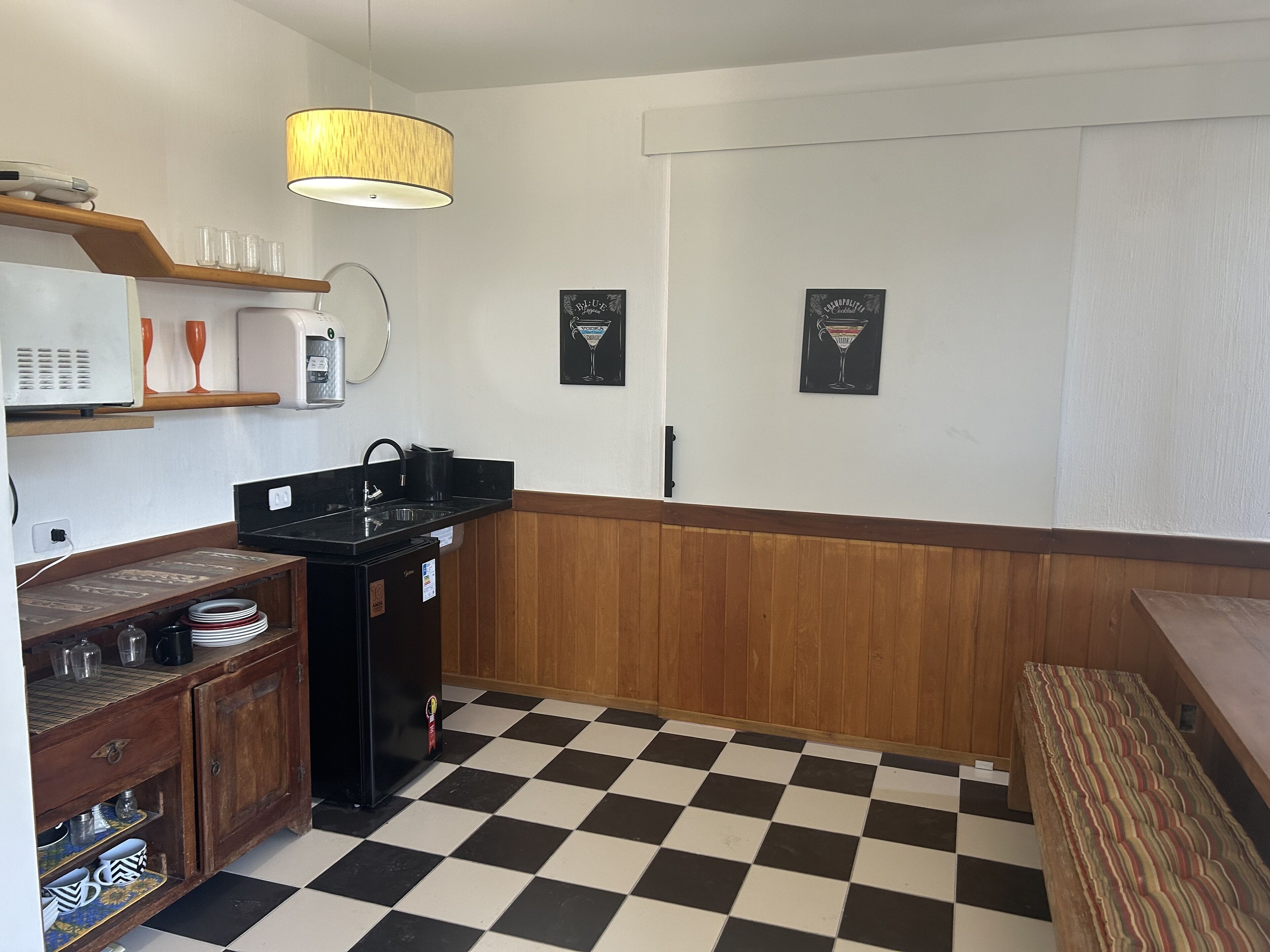 Una cocina compacta con suelo a cuadros, paneles de madera, un microondas, un fregadero y un refrigerador.