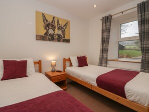 A double room with two single beds, a nightstand with a lamp, a painting of donkeys, and a window with curtains. - 8 Little Mell Fell (Penrith)