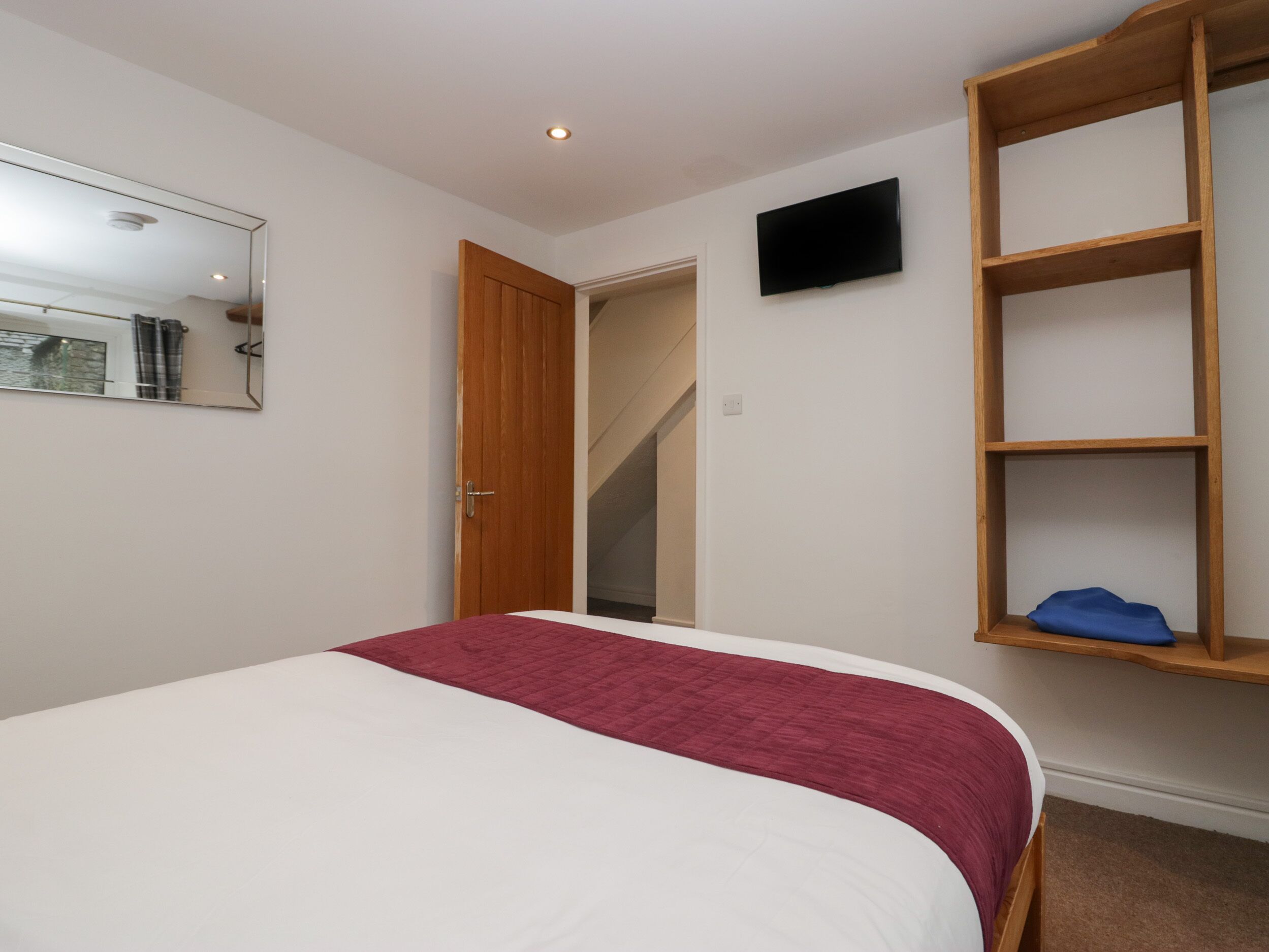 Una camera da letto con un letto, una mensola in legno, una televisione e una porta che dà su una scala.