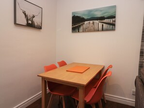 A dining area with a wooden table and orange chairs, framed artwork on the walls, and a view of a dock and water. - 8 Little Mell Fell (Penrith)