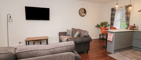 A modern living room with a grey sofa, a small wooden table, and a flat-screen TV mounted on the wall.