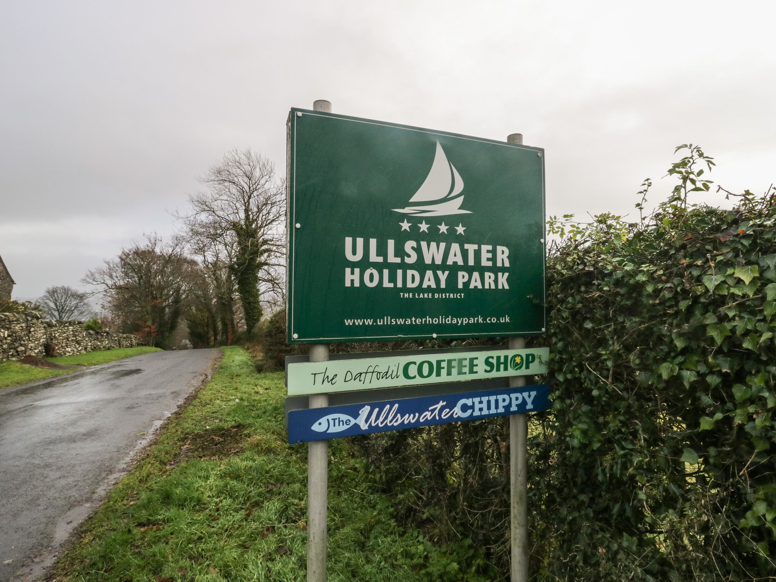 Señal para Ullswater Holiday Park, con una URL de sitio web y dos señales adicionales para The Daffodil Coffee Shop y The Ullswater Chippy.