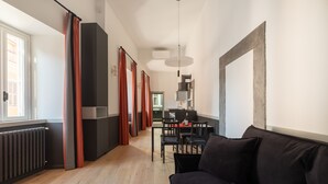 Een moderne woonkamer met een zwarte bank, houten vloeren en een eethoek met een tafel en stoelen.