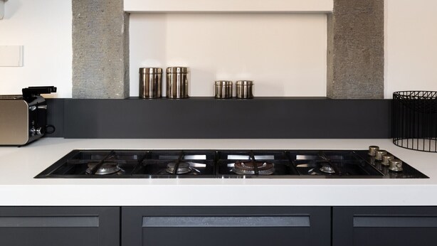 Een moderne keuken met een centraal eiland, een gasfornuis en een strakke, zwarte afzuigkap.