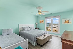 Ein Schlafzimmer mit zwei Betten, einem Deckenventilator und einem großen Fenster mit Blick auf Gebäude.