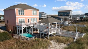 A beachfront house with a pool, a covered deck, and a staircase leading to a balcony. - 5 Bedroom Oceanfront home with private pool! (Oak Island)