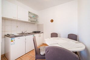A compact kitchen with white cabinets, a built-in sink, and a dining area with a table and chairs. - Apartment Near Supermarket Milo (Novalja)