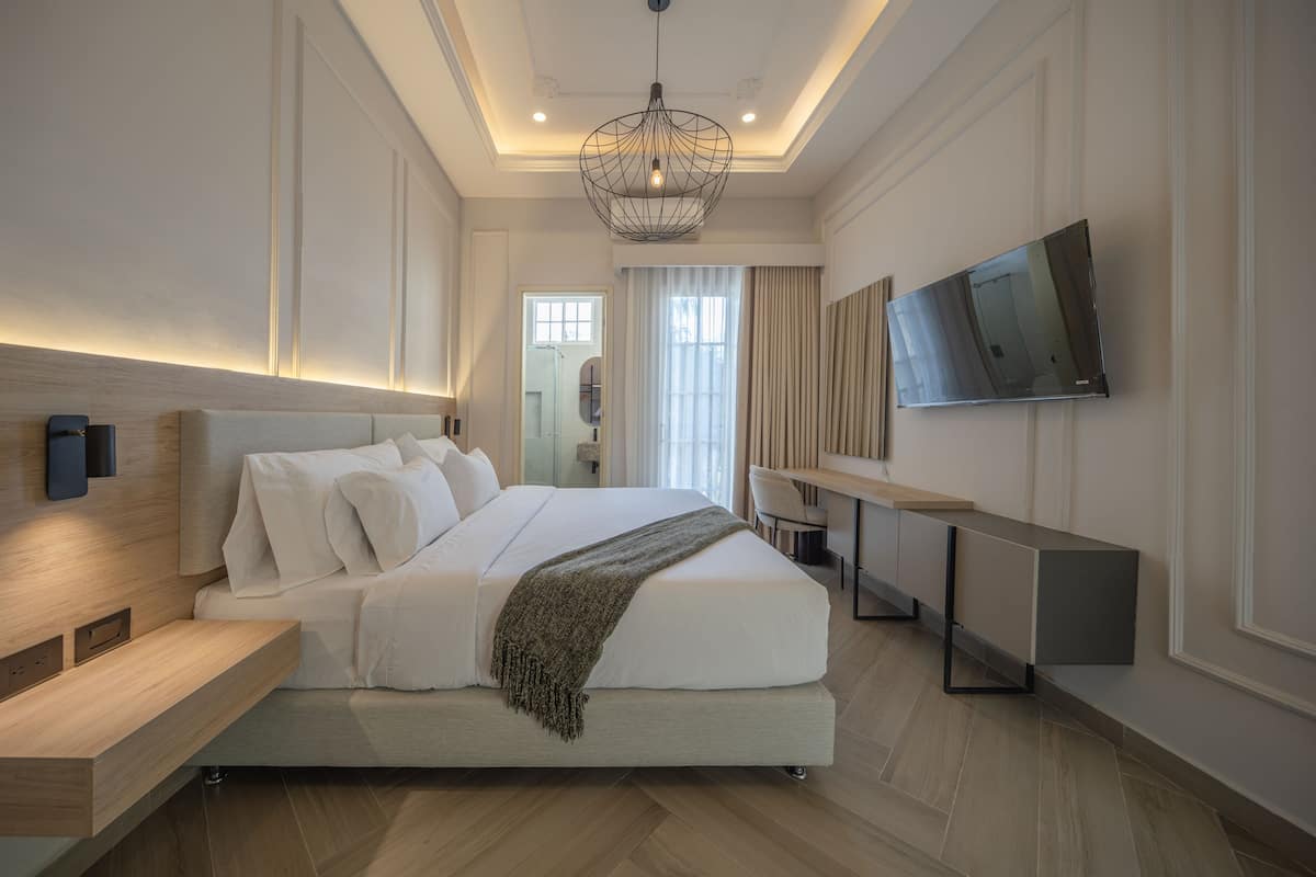 A modern hotel room with a large bed, bedside tables, a flat-screen TV, and a ceiling light fixture.