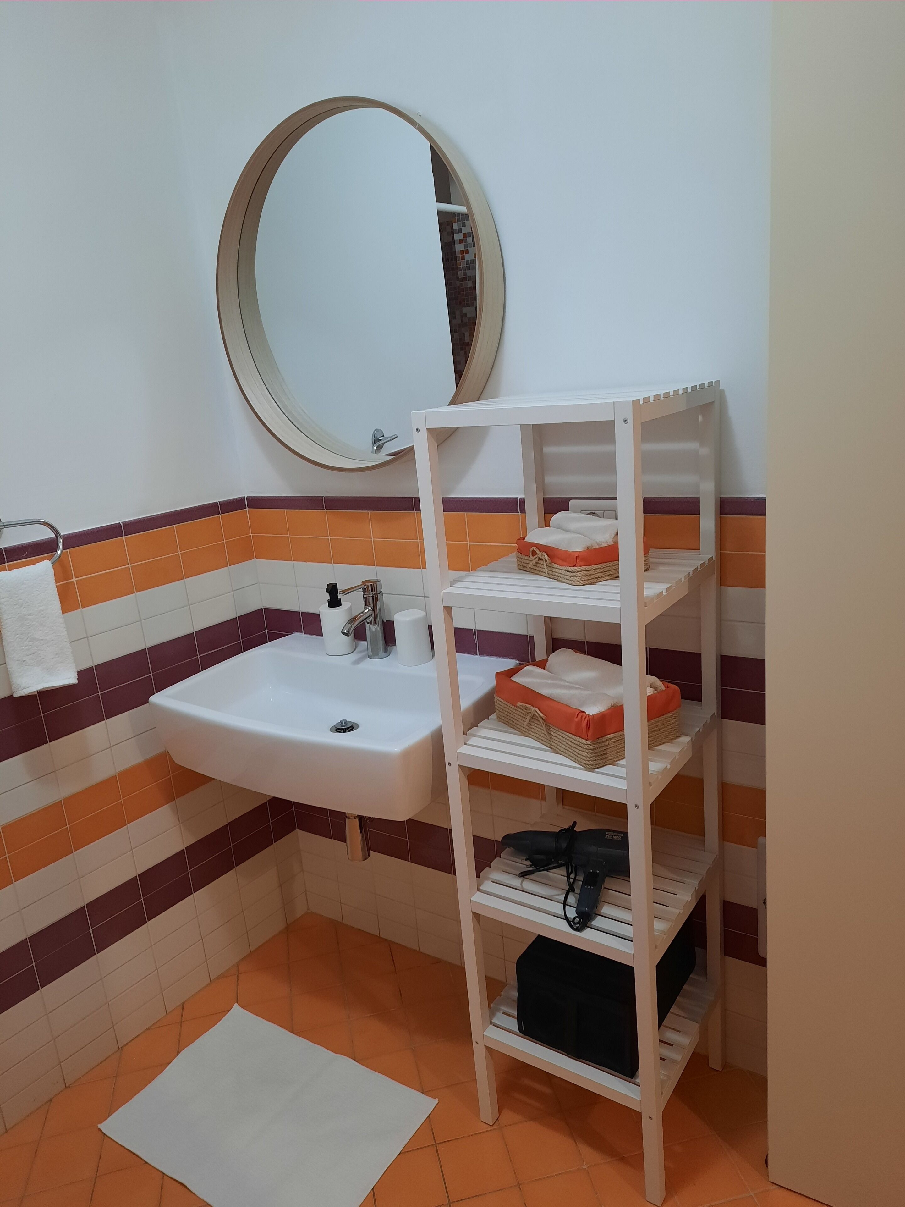 Ein Badezimmer mit einem weißen Waschbecken, einem Spiegel und einem weißen Regal mit Toilettenartikeln.