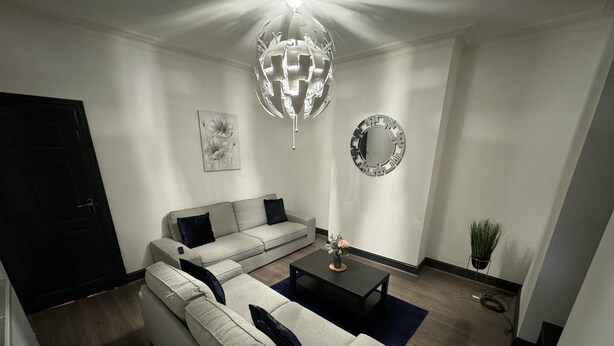 A modern living room with a sectional sofa, a coffee table, a wall clock, and a potted plant.