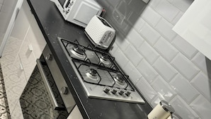 A kitchen with a gas stove, a microwave, and three labeled containers for tea, coffee, and sugar.