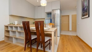 A modern kitchen with a dining area, wooden chairs, a white pendant light, and a stainless steel refrigerator.