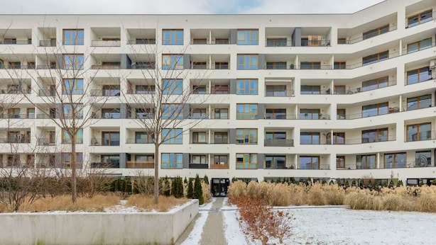A multi-story residential building with balconies, a central entrance, and a snow-covered ground.