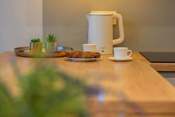 Una mesa de madera con una bandeja que contiene un pastel, una cafetera blanca y dos tazas blancas.