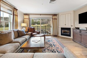 A living room with a sofa, a wooden coffee table, a fireplace, a television, and a view of the outdoors. - Mountain Vista 3-BR Haven at Jackson Gore Resort (Ludlow)