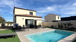 Una casa moderna con piscina, un patio con mobiliario exterior y un césped bien cuidado.