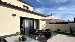 Un patio al aire libre con mesa de vidrio, sillas y una sombrilla grande.