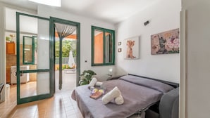 A bedroom with a bed, a window, a painting, and a view of the outside.