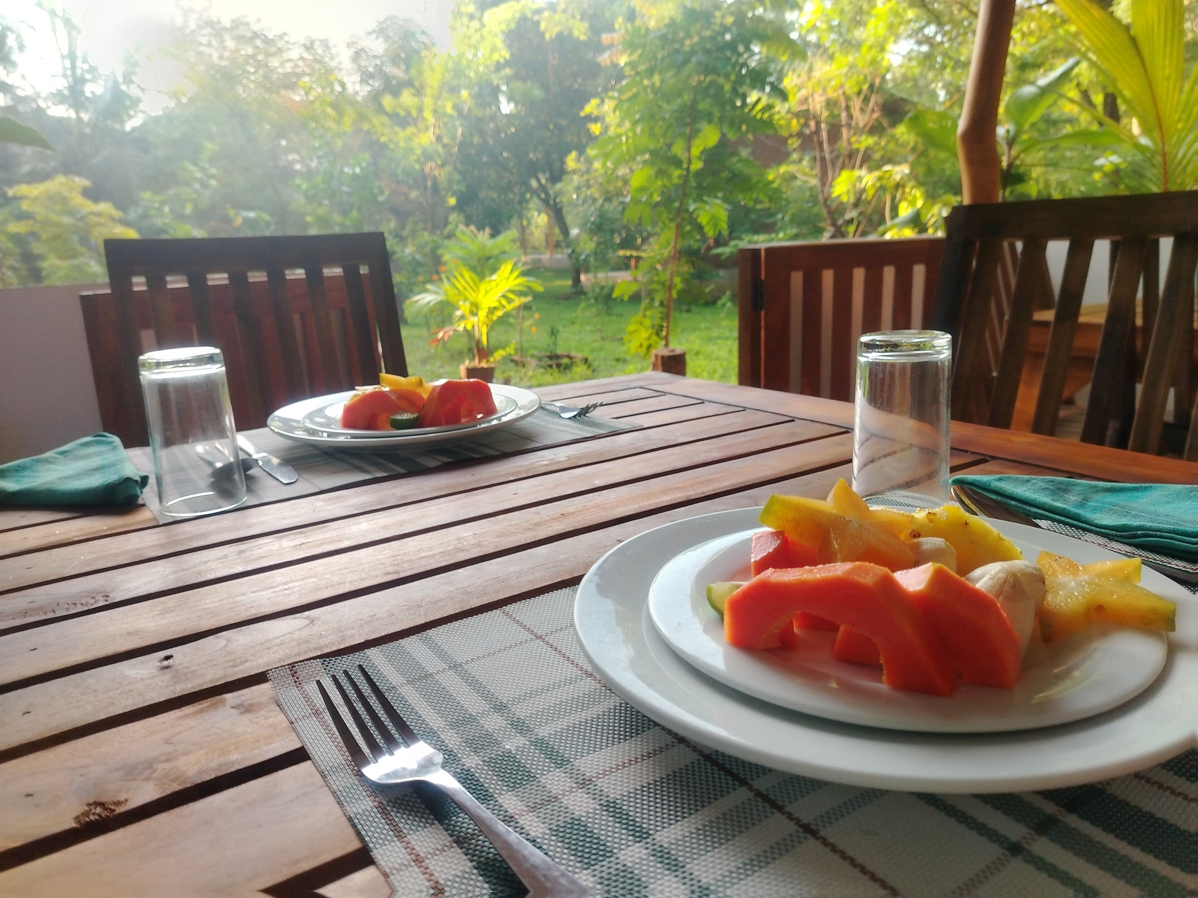 Une table en bois avec un set de table, deux assiettes de fruits, un verre d’eau et une fourchette.