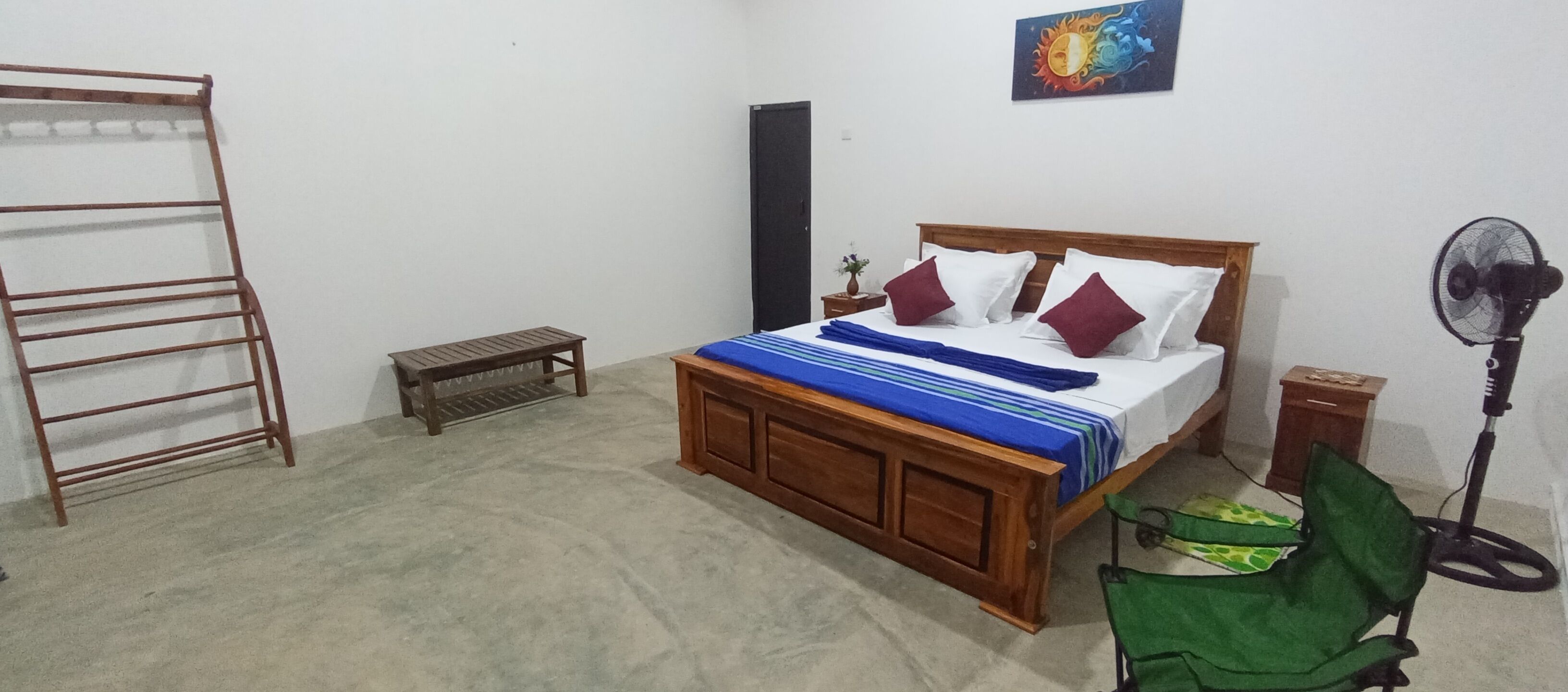 Een slaapkamer met een houten bed, een bankje, een ventilator en een trap.