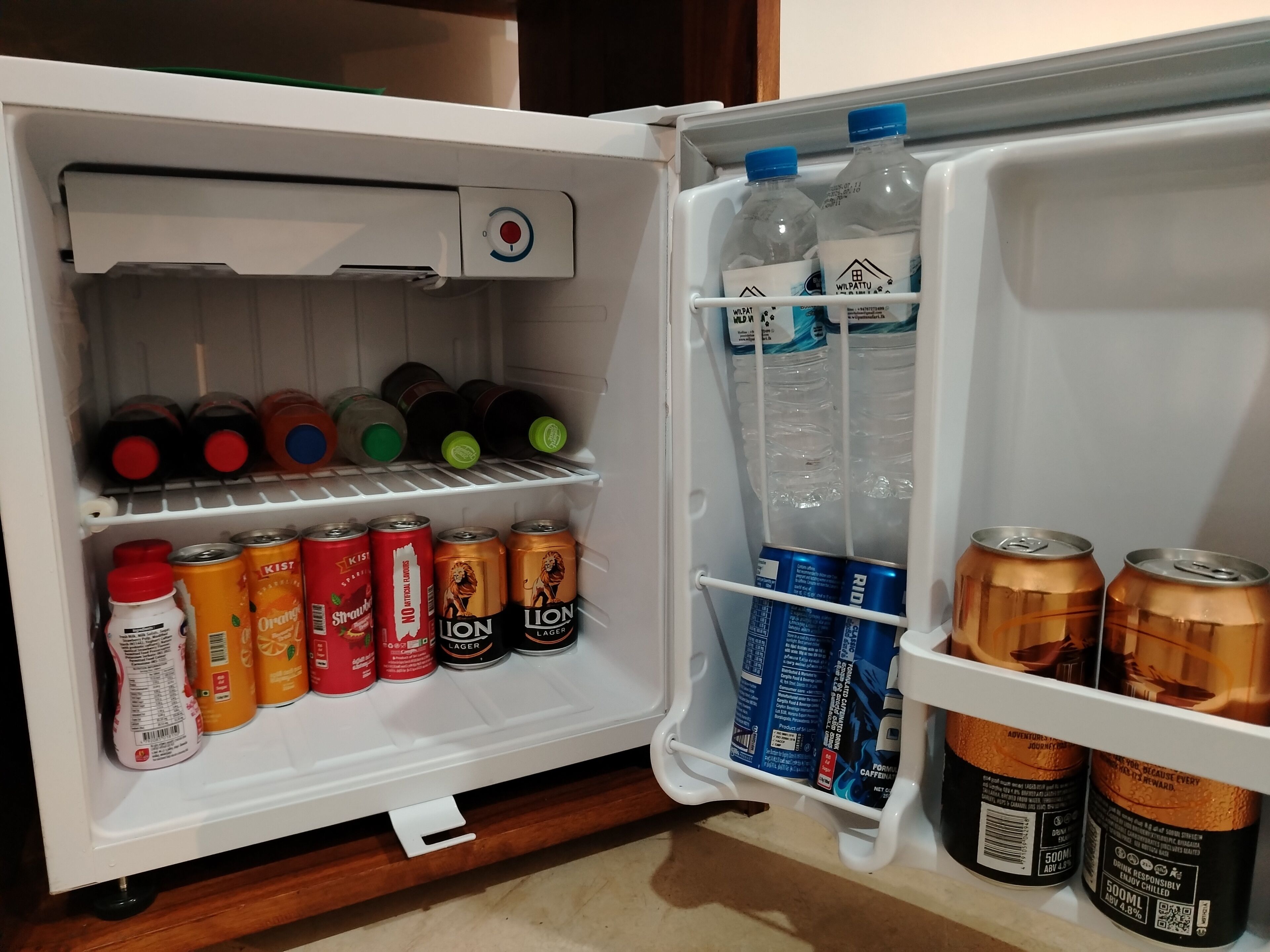 A refrigerator with various beverages and cans, including brands like KIST, STRANW, and LION.