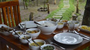 Une table à manger dressée avec différents plats et couverts, entourée d’un cadre naturel en plein air.