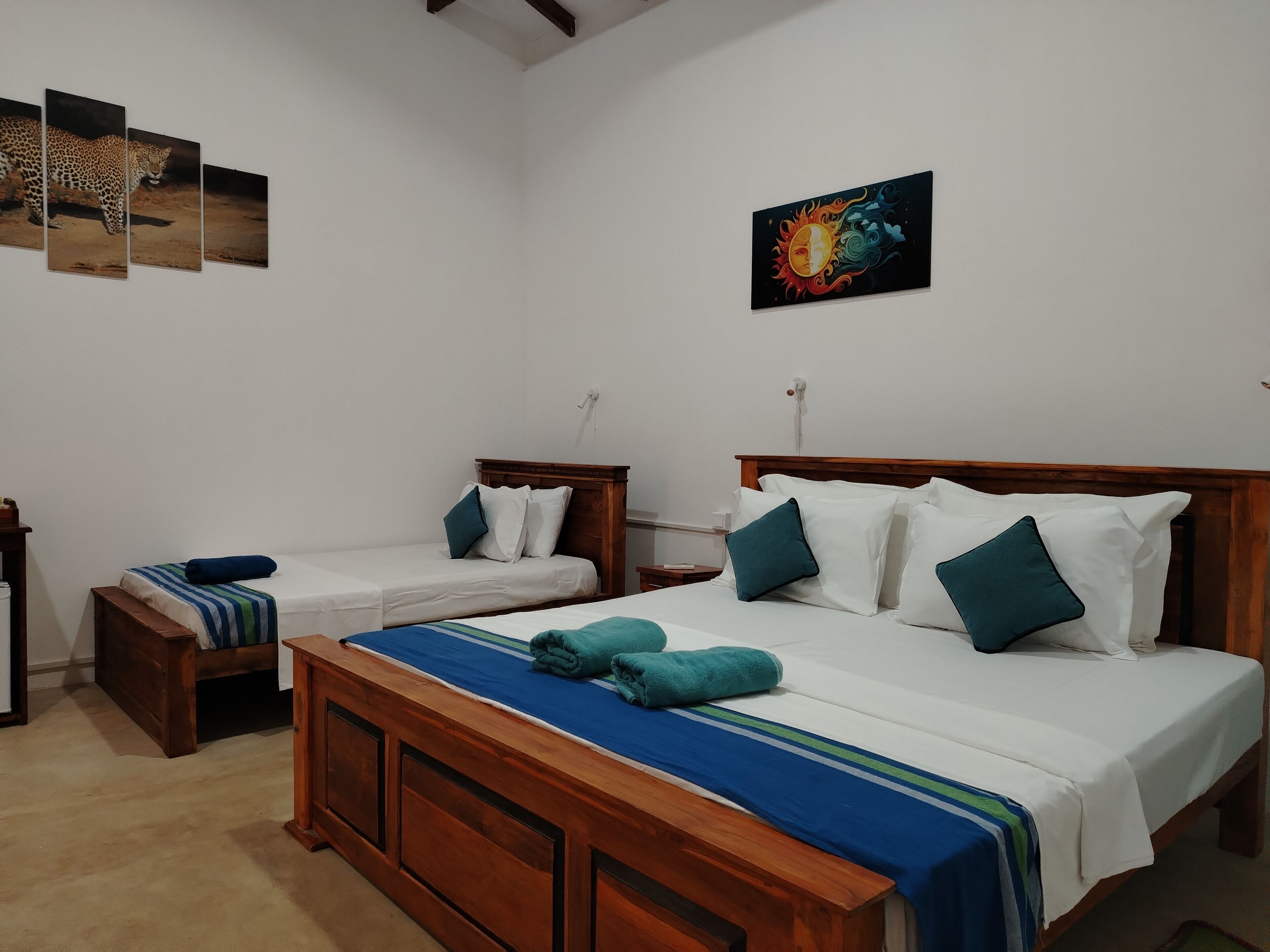 Une chambre d’hôtel avec un grand lit, deux petits lits, des têtes de lit en bois et un banc en bois.