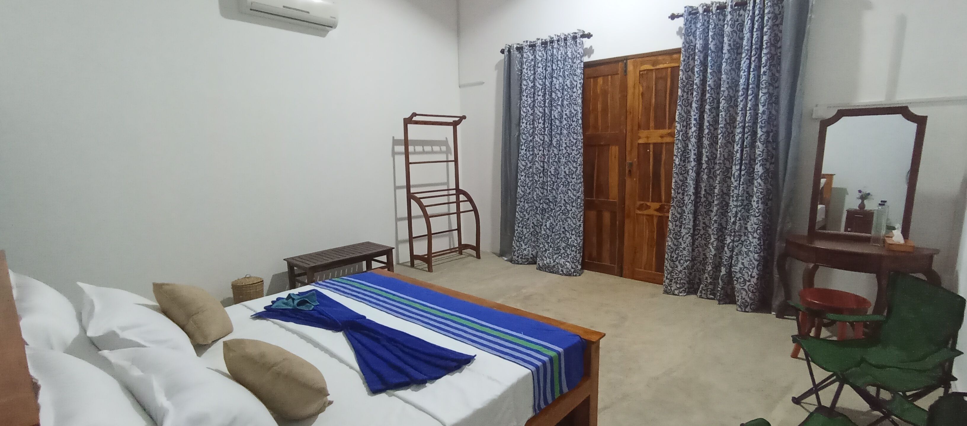 Une chambre à coucher avec un lit, une chaise en bois, une petite table, un miroir et une armoire.