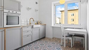 Une cuisine moderne avec des meubles blancs, un four encastré, un évier et une fenêtre donnant sur un paysage urbain.