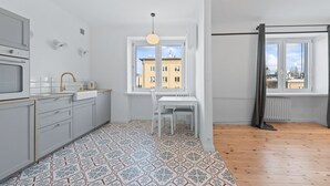 Une cuisine moderne avec des meubles blancs, un plan de travail blanc et un sol à motifs. Une fenêtre offre une vue sur les bâtiments environnants.