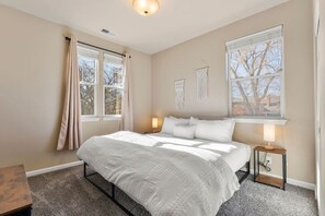 Une chambre à coucher comprenant un lit, deux tables de chevet, une fenêtre et une décoration murale en macramé.