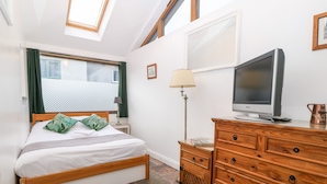A bedroom with a bed, wooden dresser, TV, and a window with curtains.
