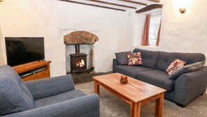 A cozy living room with a stone fireplace, a sofa set, a wooden coffee table, and a television.