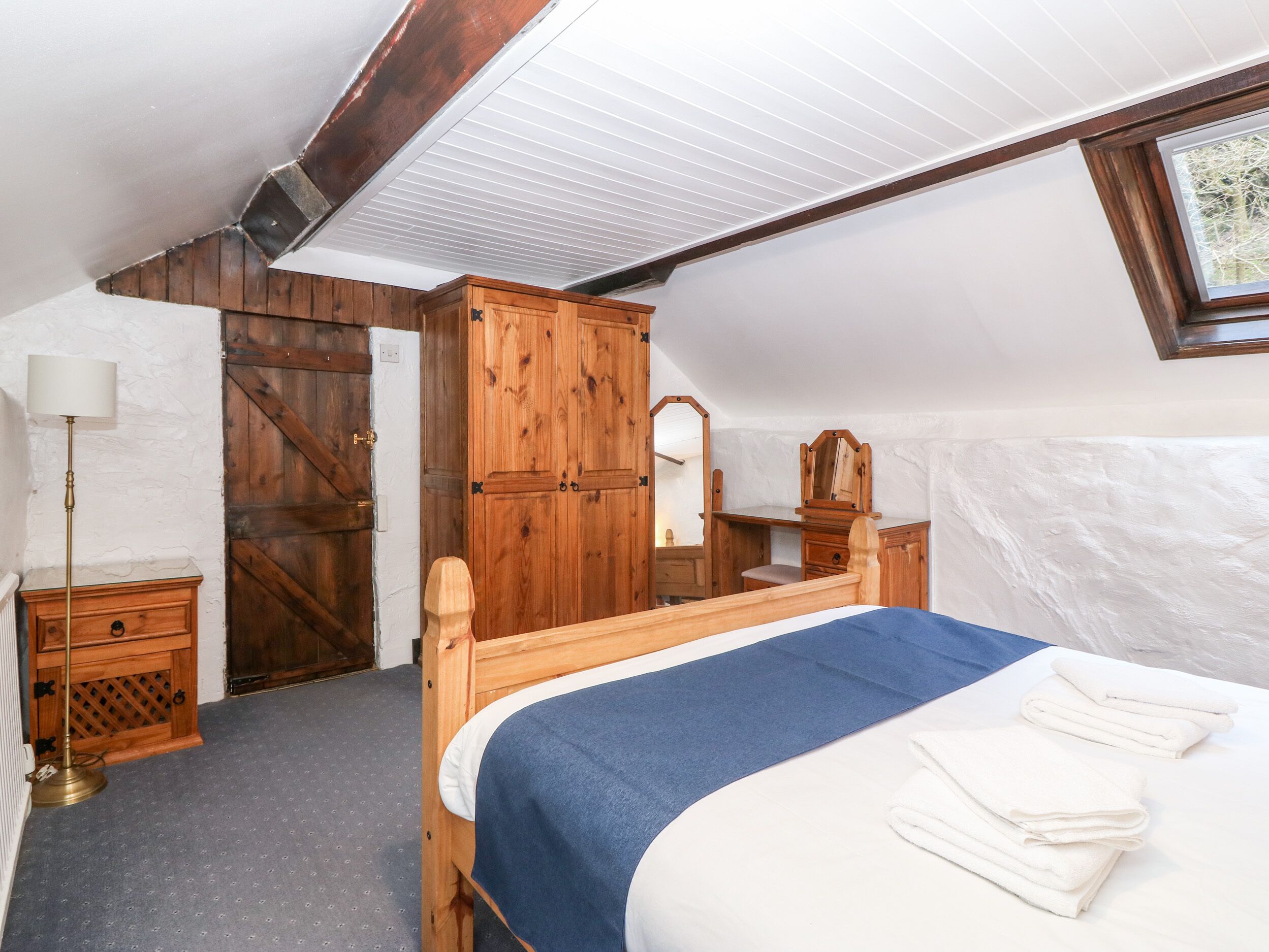 A bedroom with a wooden bed, a dresser, a mirror, and a wardrobe.