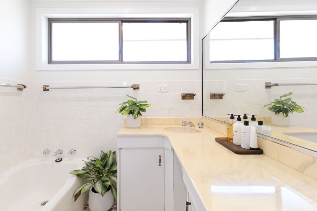 A modern bathroom with a bathtub, a vanity with a mirror, and potted plants.